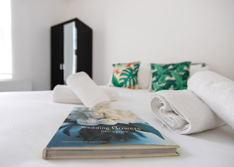 Bedroom with white bed, rolled towels, decorative pillows, black wardrobe and book on surface