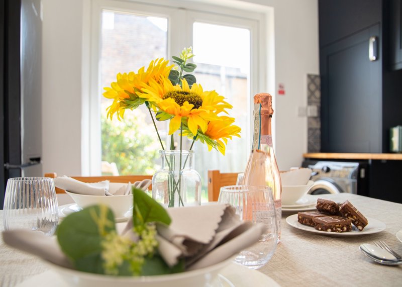 Modern kitchen dining area with yellow flowers, wine bottle, place settings and window view
