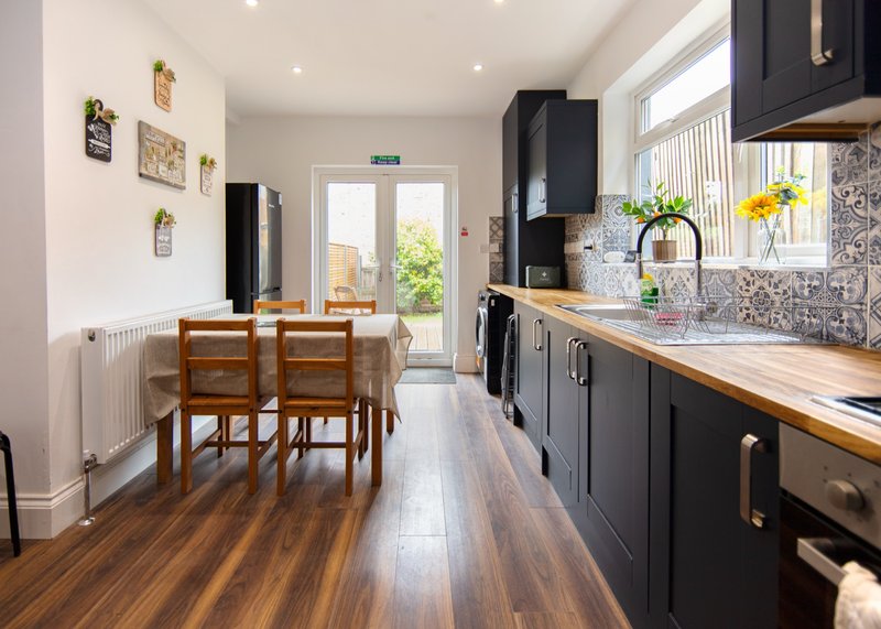 Modern kitchen with black cabinetry, wooden countertops, and dining area with wooden chairs