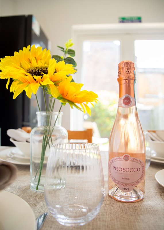 Dining table with yellow gerbera flowers in vase, prosecco bottle, and place settings