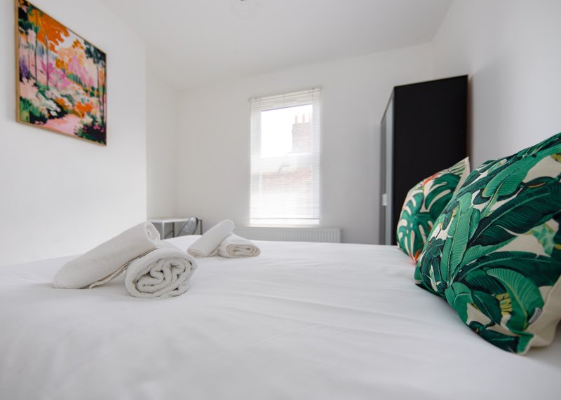 Bright bedroom with white bed, green patterned blanket, colorful wall art and window