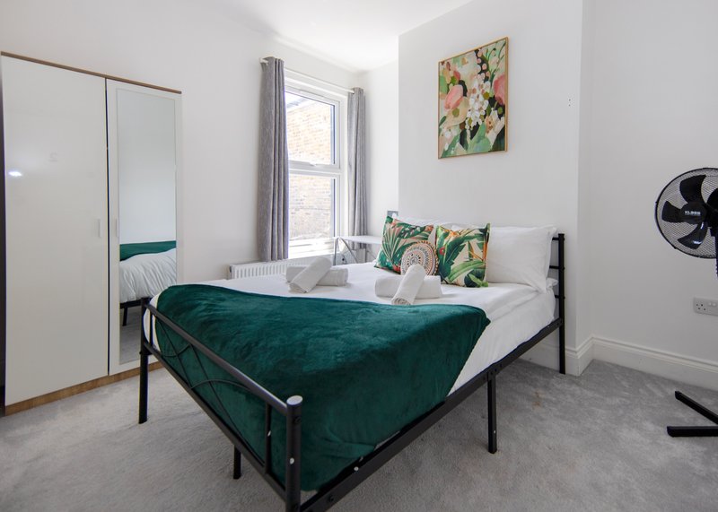 Bedroom with double bed, green velvet bedding, white wardrobe, and window with curtains