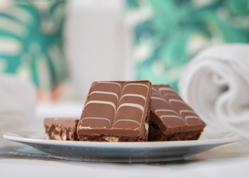 Chocolate brownies on white plate with plant and rolled towel in background