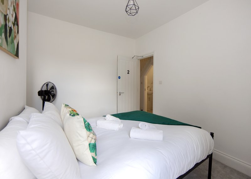 Bedroom with double bed, white bedding, green throw, small fan, and pendant light fixture