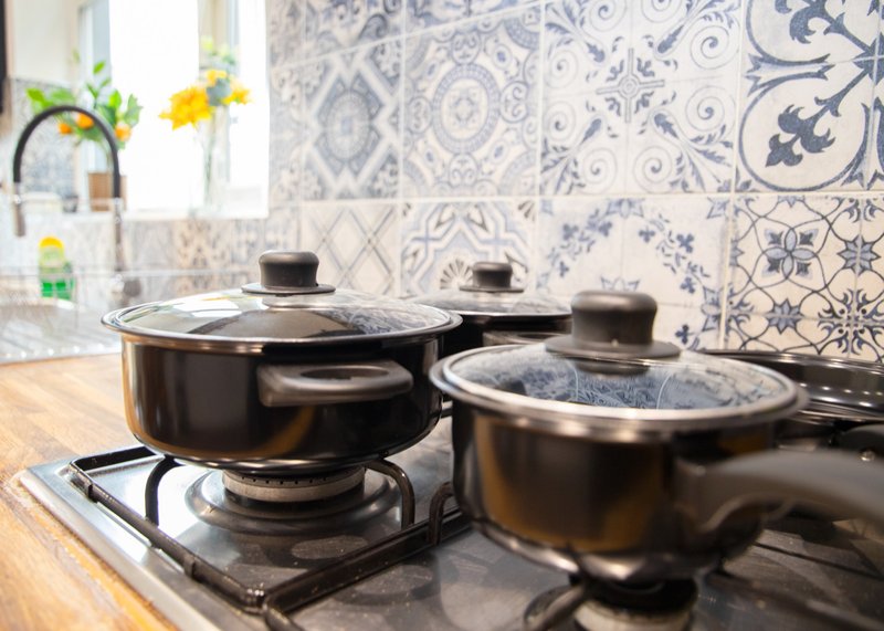 Kitchen stovetop with two black pots, blue and white patterned backsplash, and window with plants