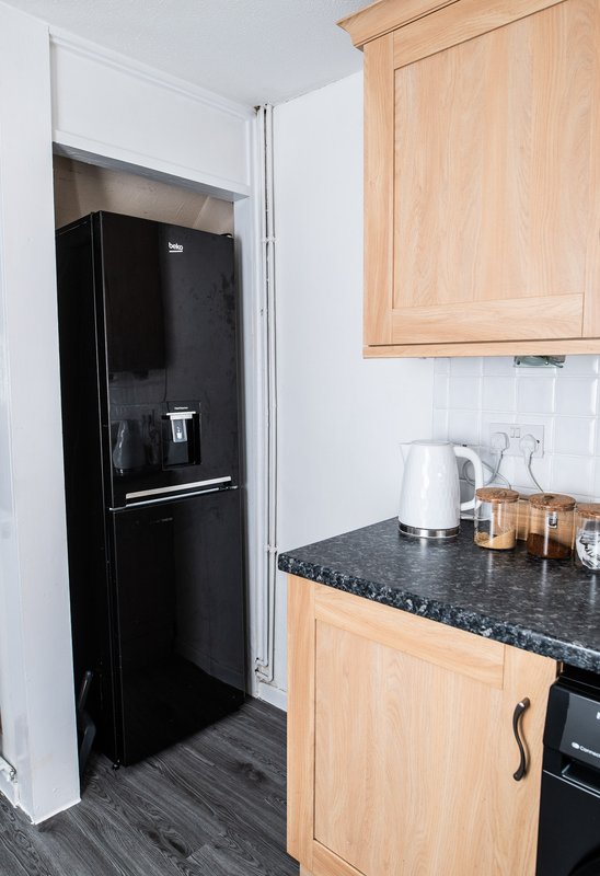 Kitchen with black fridge, wooden cabinets, granite countertop, kettle and storage jars
