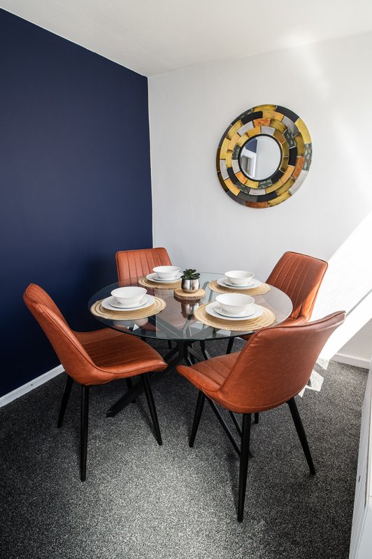Modern dining nook with round black table, orange chairs, place settings and decorative mirror