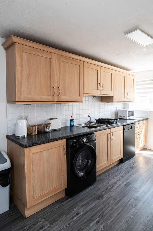 Modern kitchen with wooden cabinets, black countertop, integrated appliances and white tile backsplash