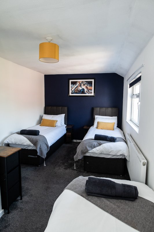 Bedroom with three single beds, dark blue accent wall, orange pendant light and window