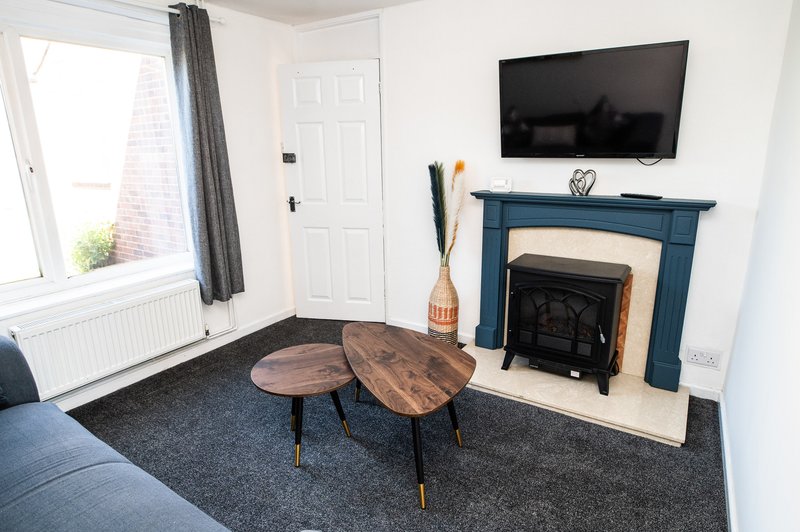 Living room with wooden coffee table, fireplace, TV mounted on wall, and grey carpet