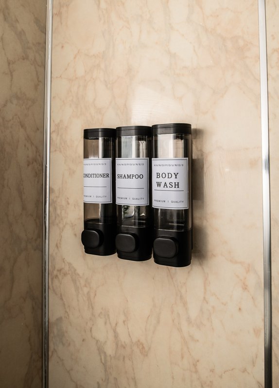 Bathroom wall with marble tiles and three-chamber dispenser containing toiletries