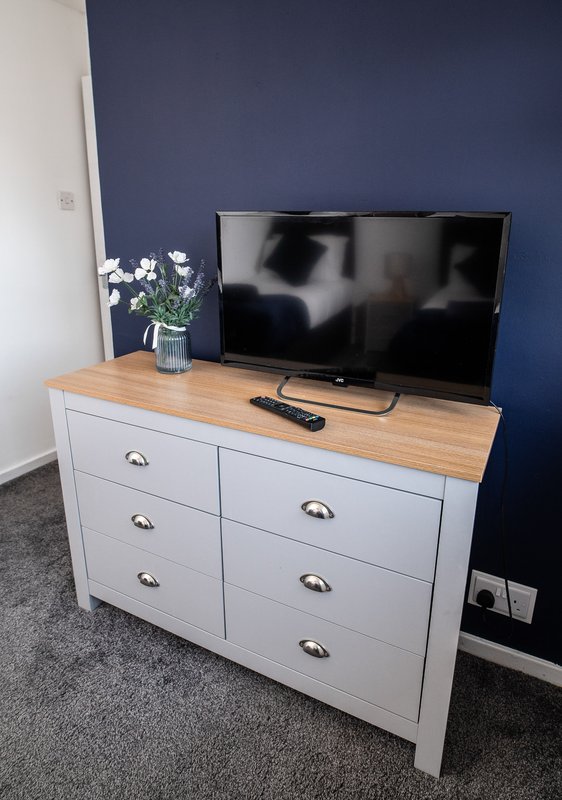 Bedroom with white dresser, wooden top, TV, flowers, and navy accent wall