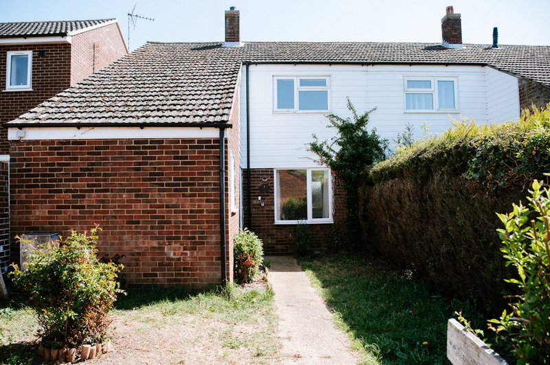 Semi-detached brick and white house with garden pathway and hedge borders