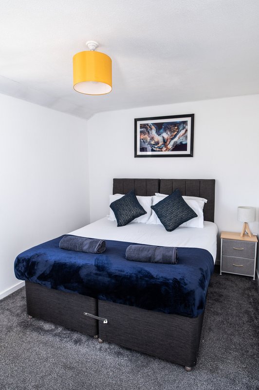 Modern bedroom with double bed, dark headboard, blue velvet throw, yellow ceiling lamp
