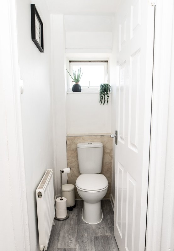 Compact bathroom with toilet, small window with plants, white walls and gray floor