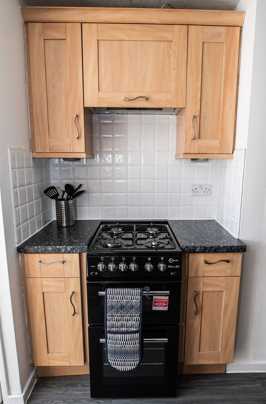 Compact kitchen with wooden cabinets, black gas range cooker, and white tile backsplash