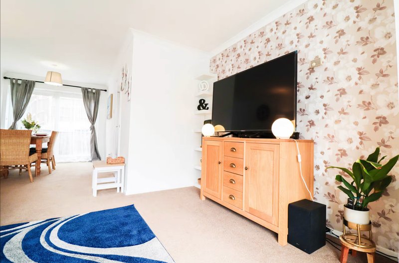 Living room with blue patterned rug, wooden TV unit, flat-screen TV, and floral wallpaper