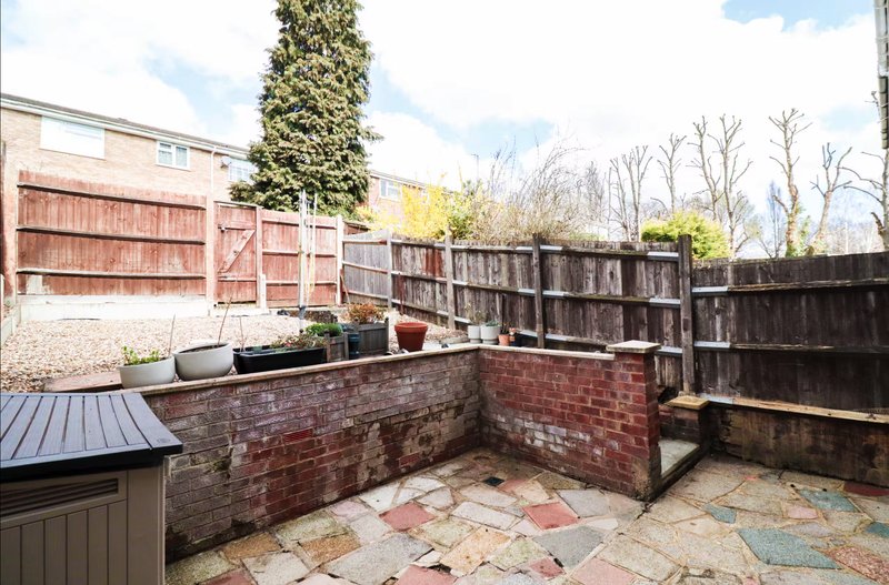 Brick-walled garden patio with stone flooring, wooden fencing, and planted containers