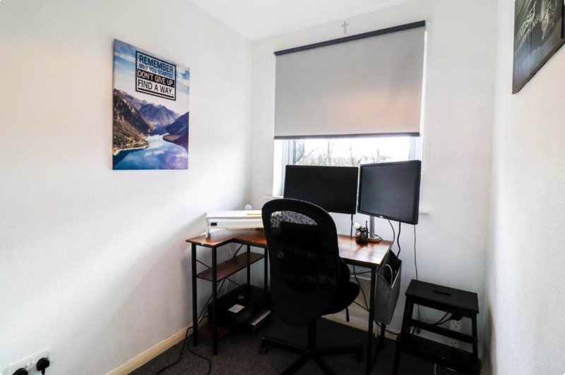 Small home office with desk, dual monitors, black chair and landscape wall art