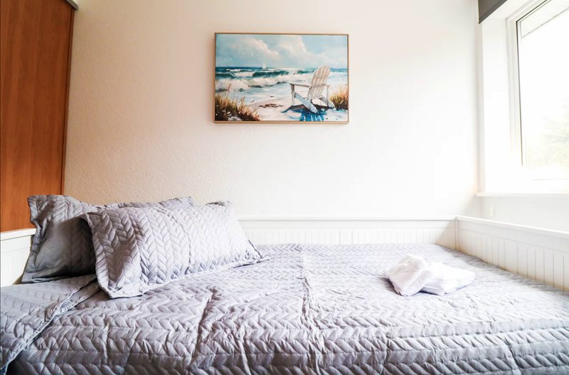 Bright bedroom with double bed, quilted bedding, pillows, and beach-themed wall art