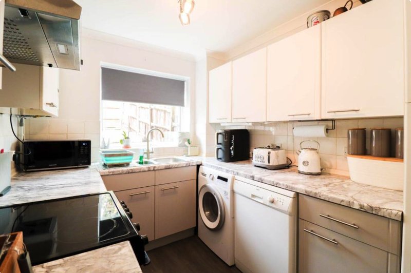 Modern kitchen with cream cabinetry, marble countertops, integrated appliances and window