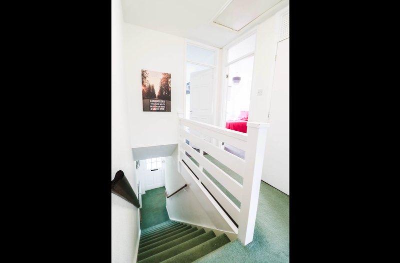 Bright hallway with stairs, white walls, storage drawers and bedroom doorway visible