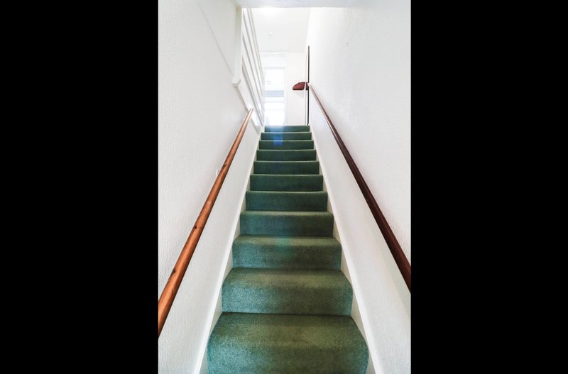 Narrow staircase with green carpet, wooden handrails, and skylight above