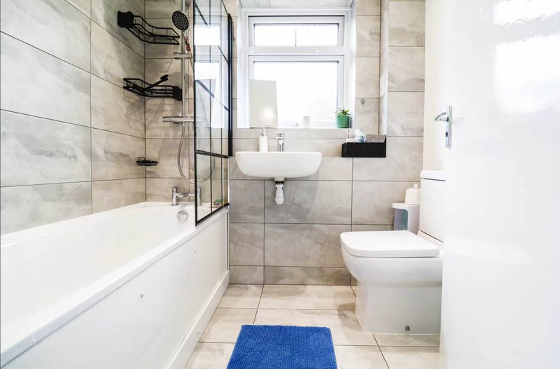 Modern bathroom with bathtub, shower enclosure, sink and toilet, blue mat