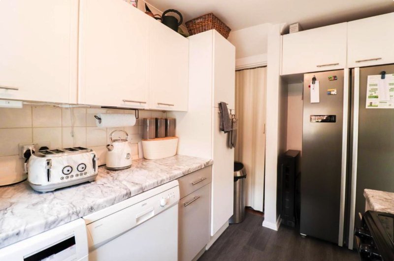 Modern kitchen with white cabinetry, marble countertop, stainless steel appliances and dark flooring