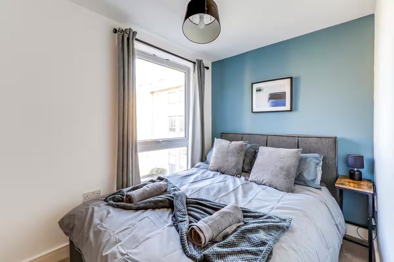 Modern bedroom with double bed, blue accent wall, wooden nightstand and ceiling light