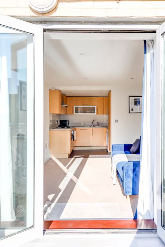 Open-plan kitchen and living area viewed through glass doors, with wooden cabinetry and blue furnishings