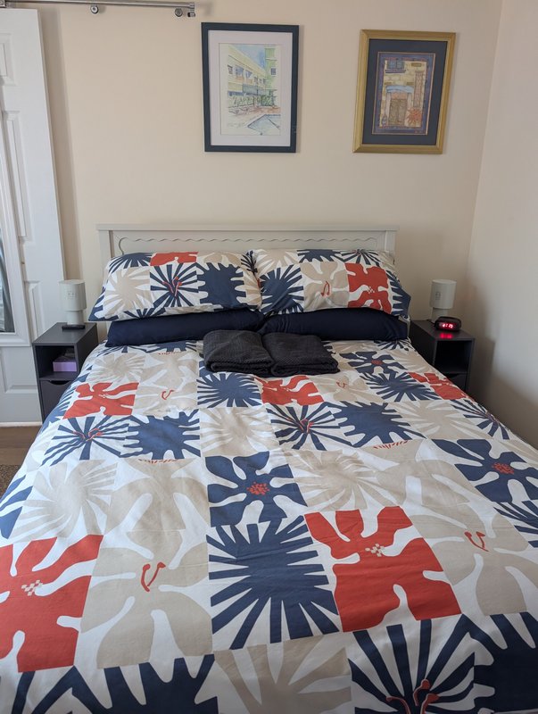 Bedroom with double bed, patterned bedding, framed wall art, bedside tables, lamps, and alarm clock
