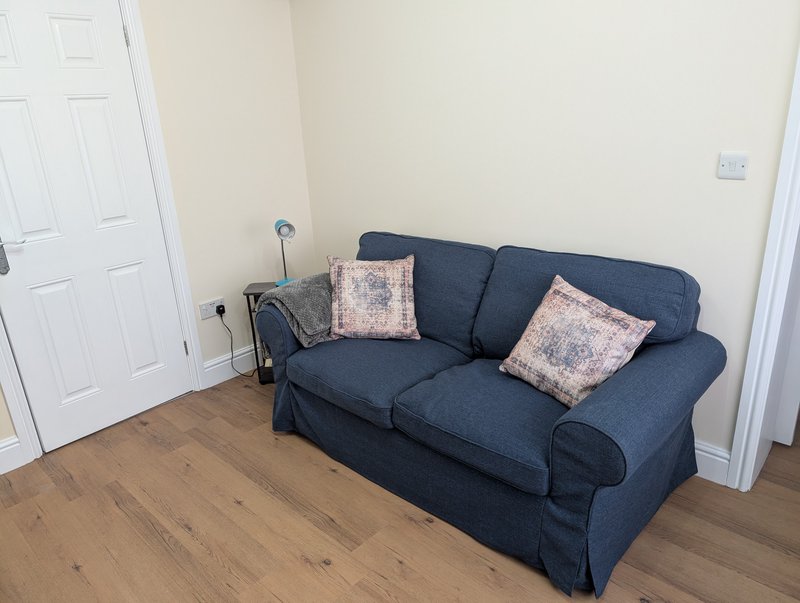 Living room with dark blue upholstered sofa, patterned cushions, wooden floor and white doors
