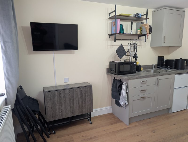 Diner kitchenette with wall-mounted TV, shelving, microwave, and wooden flooring