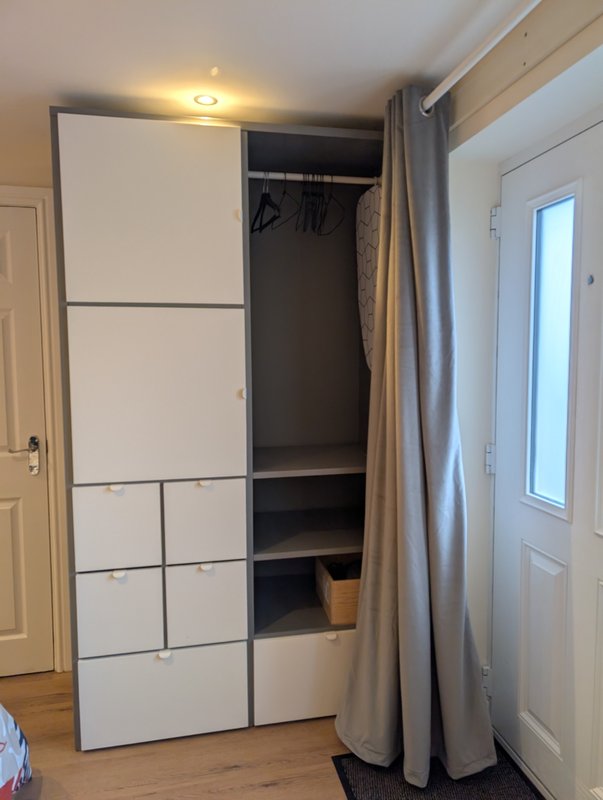 Bedroom with white modular storage unit, hanging rail, ironing board, and iron and hairdryer (in box).