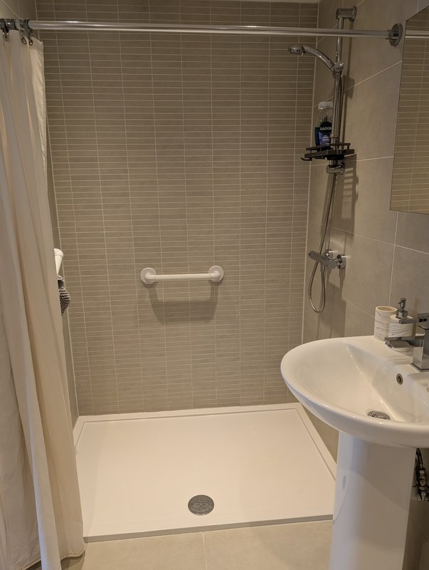 Modern bathroom with walk-in shower, pedestal sink and tiled walls. Shower seat available on request.