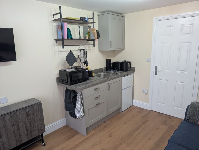 Modern kitchenette with gray cabinetry, shelving, wooden flooring, and white door