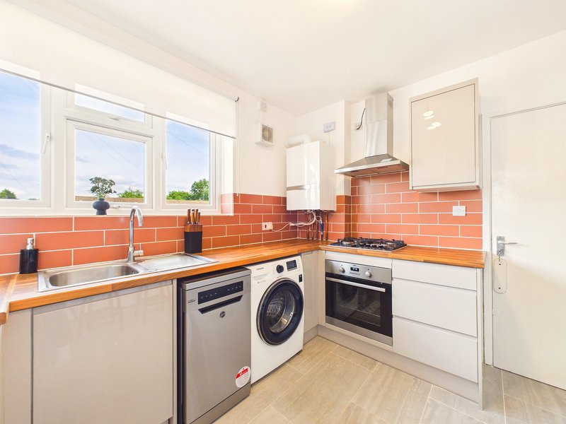Modern kitchen with orange tile backsplash, white cabinetry, stainless steel appliances and windows