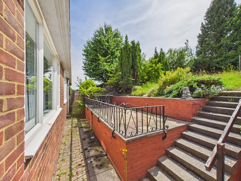 Brick exterior with patio, raised planters, metal railing and garden steps beyond