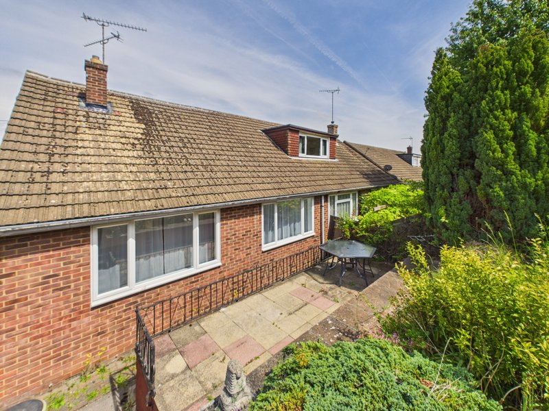 Brick bungalow with tiled roof, patio area, and mature garden shrubs