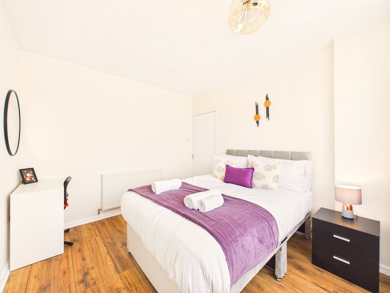 Bright bedroom with double bed, purple bedding, wooden floor and bedside table