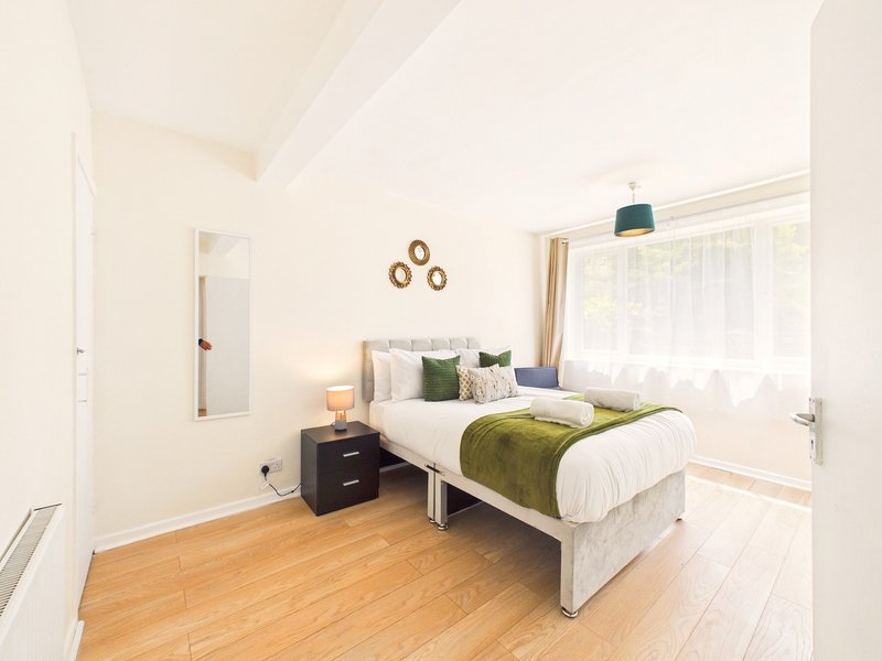 Bright bedroom with double bed, wooden floor, black bedside table and window with curtains
