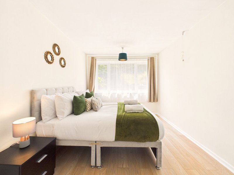 Bright bedroom with double bed, bedside table, lamp, and window with beige curtains
