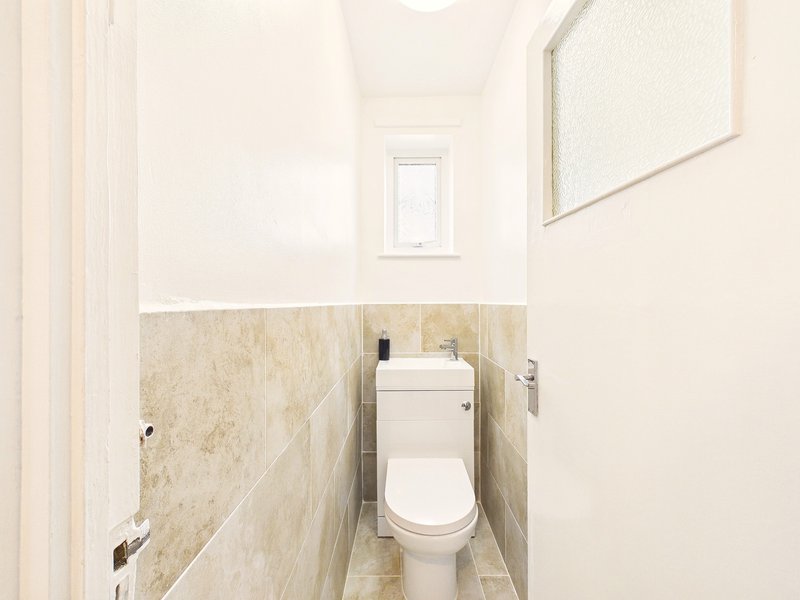 Clean bathroom with toilet, beige tile walls, mirror, and small window