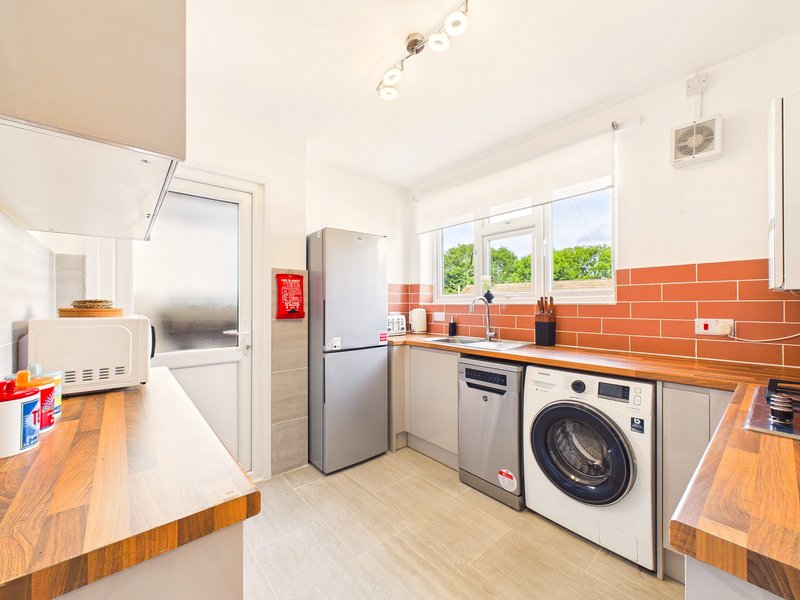 Modern kitchen with wooden countertops, stainless steel appliances, orange brick backsplash and natural light