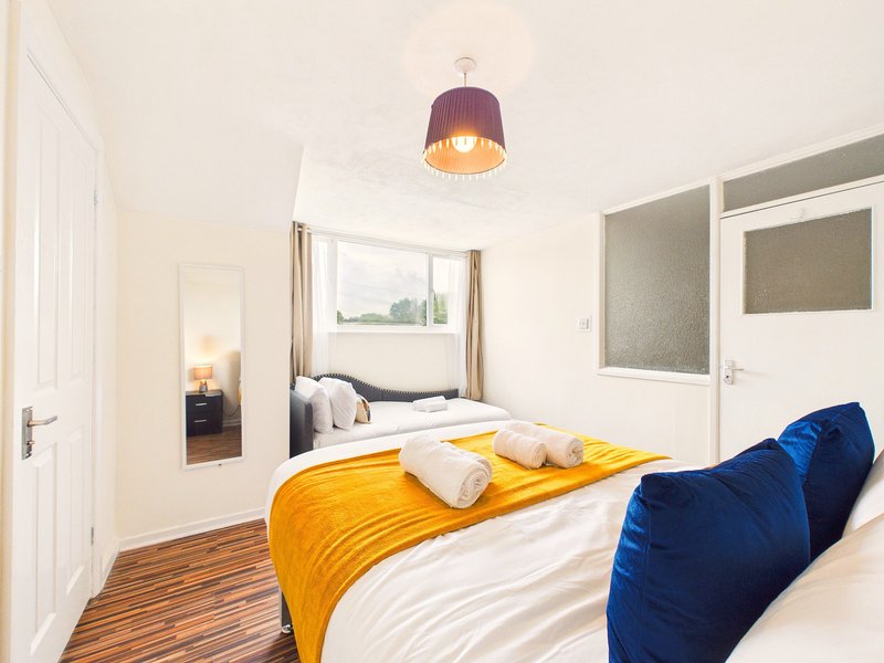 Modern bedroom with double bed, yellow throw, blue cushions, pendant lamp and wooden flooring