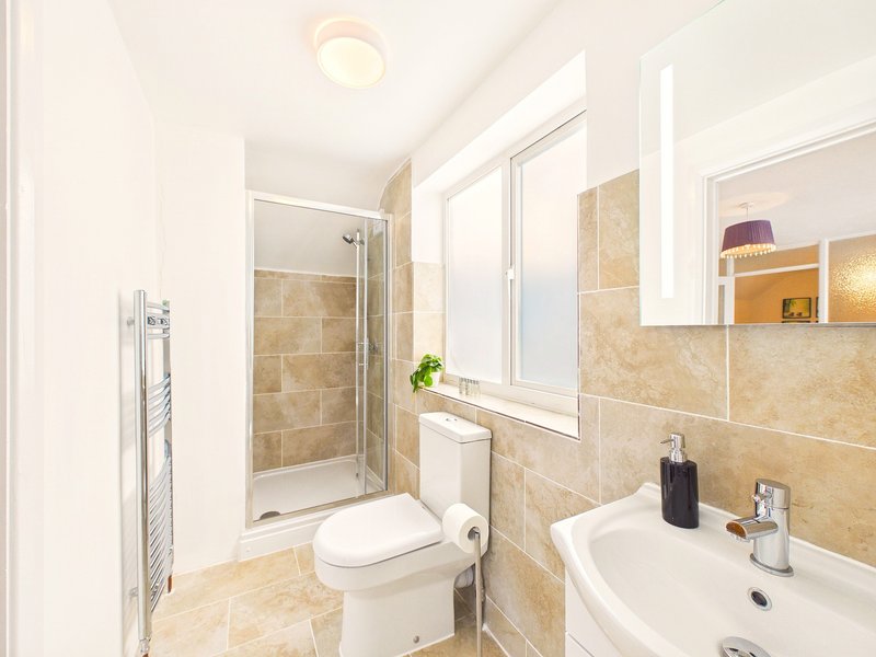 Modern bathroom with shower enclosure, toilet, sink, heated towel rail and window