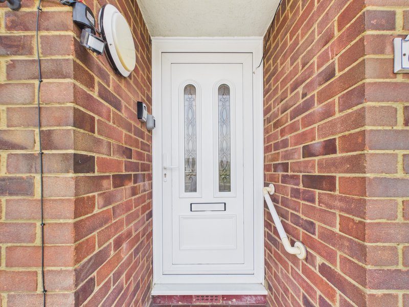 White front door with glass panels set between red brick walls