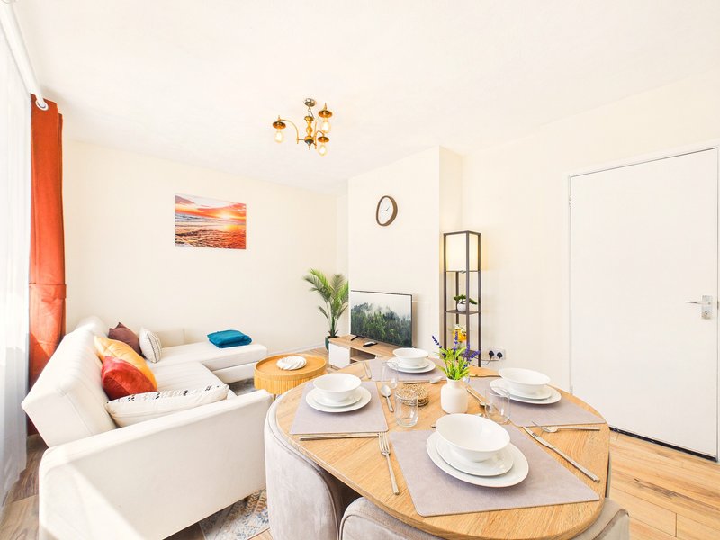 Open-plan living and dining area with cream sofa, wooden dining table set for four, and potted plants