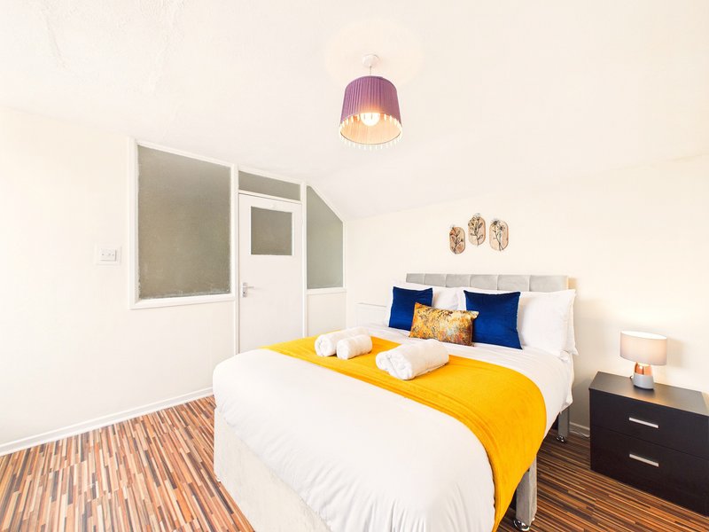 Bedroom with double bed, yellow throw, blue pillows, wooden floor and purple pendant lamp